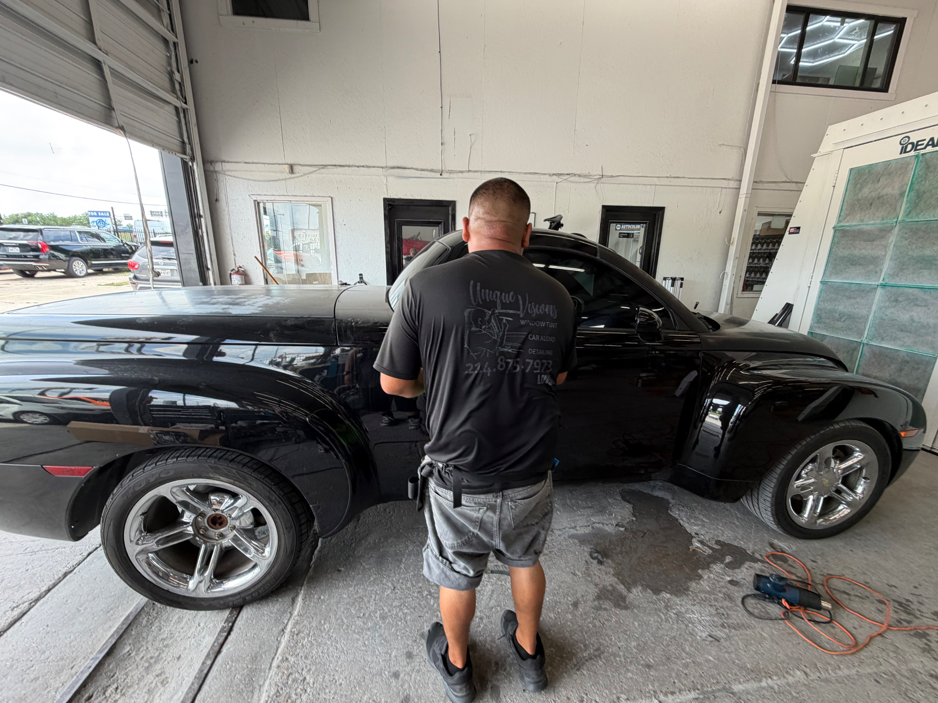 A Unique Visions team member working beside a black custom coupe in the studio.