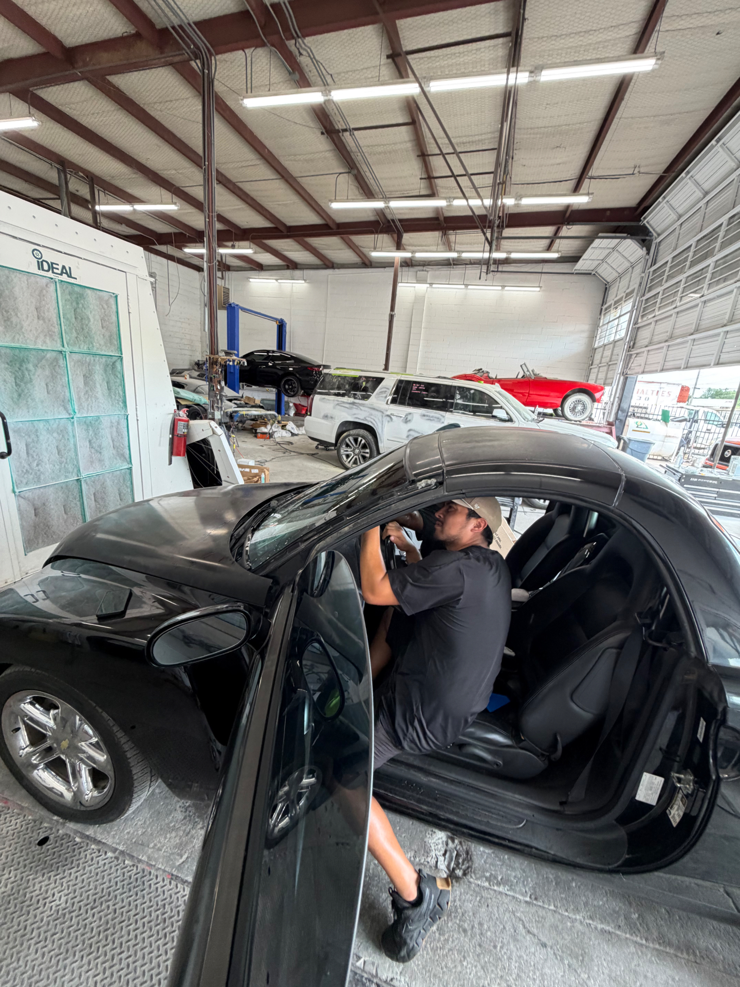 Unique Visions technician applying window tint to a black coupe inside the Dallas shop.