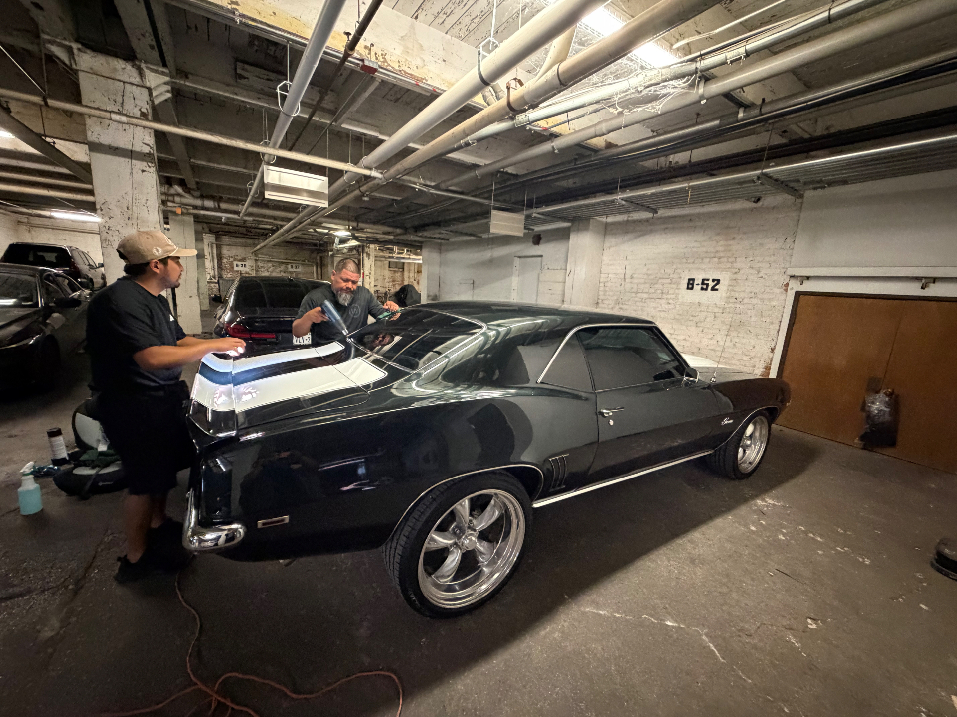 Two technicians refining the finish on a classic dark coupe in an indoor garage setting.